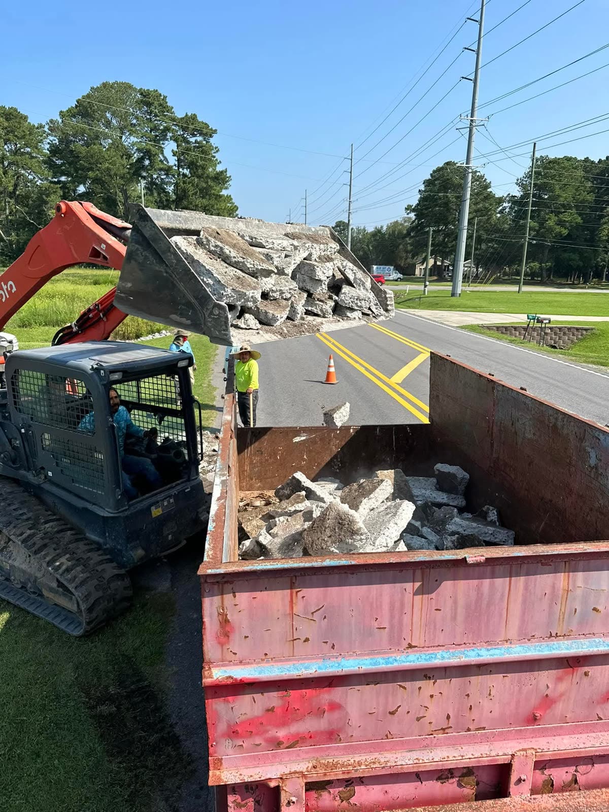 Crew loading broken concrete into an Express Waste roll-off dumpster with a track loader
